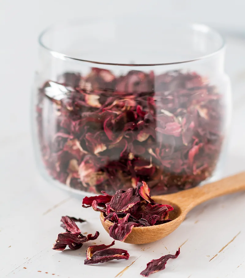 hibiscus séché origine du Mali dans un verre transparent posé sur une table à côté d'une cuillère en bois
