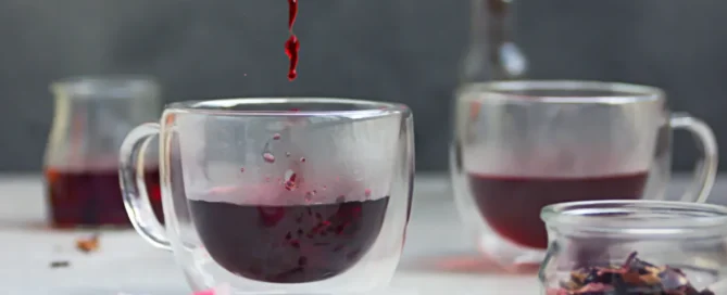 tasse transparente avec décoction d'hibiscus versée dedans et au première plan des fleurs d'hibiscus