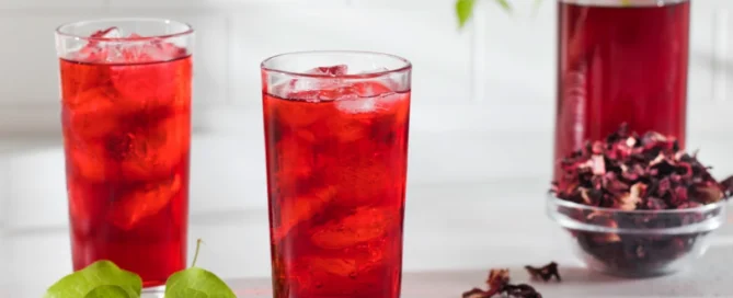 Infusion à froid d'hibiscus avec 2 verres de bissap ainsi qu'une bouteille posés sur une table avec des fleurs séchées dans un bol