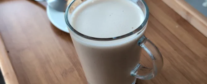 Un latte au baobab posé sur un plateau en bois avec une part de crumble aux pommes derrière