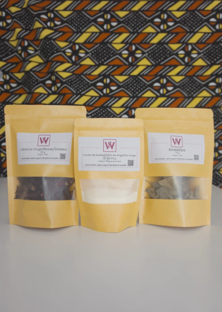 3 sachets en kraft posés sur une table blanche, chaque sachet contient de l'hibiscus de la poudre de baobab et du kinkéliba