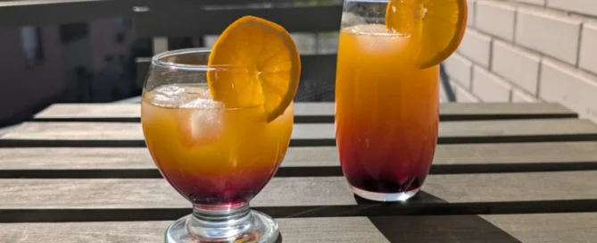 deux verres d'hibiscus sunrise cocktails sans alcool hibiscus posés sur une table en bois sur un balcon