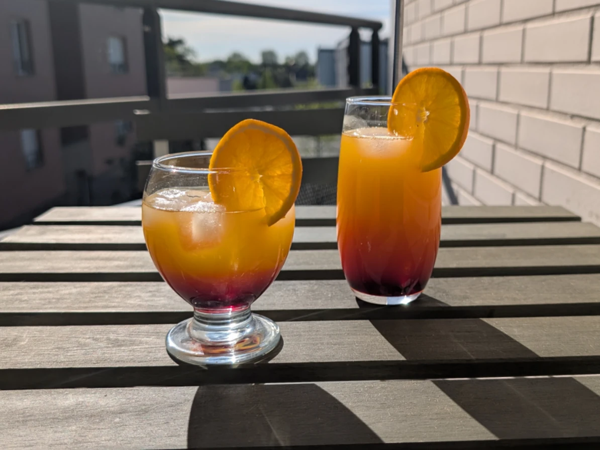 deux verres d'hibiscus sunrise cocktails sans alcool hibiscus posés sur une table en bois sur un balcon